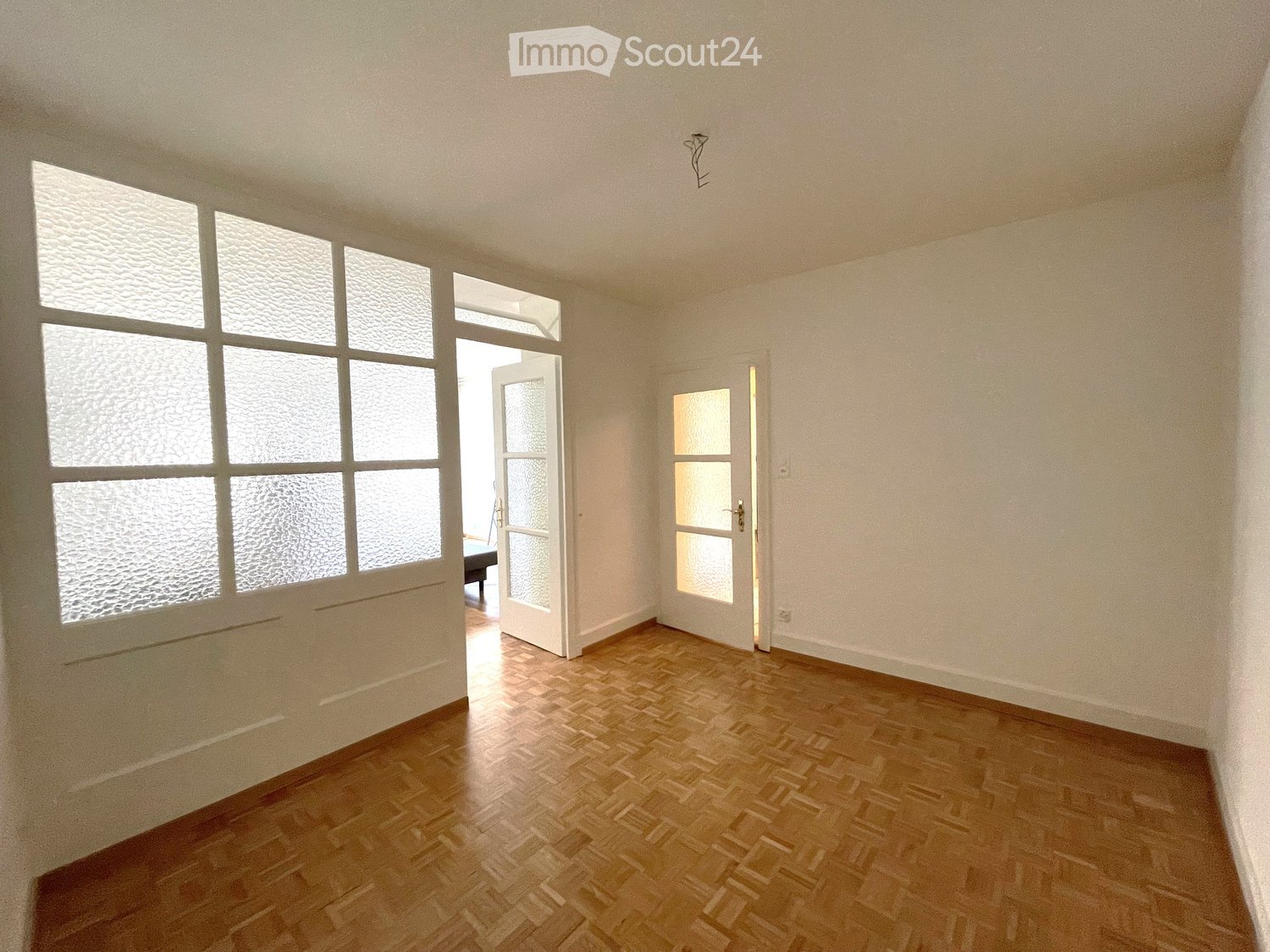 Empty room with wooden flooring, large frosted windows, and two open doors leading to other spaces.