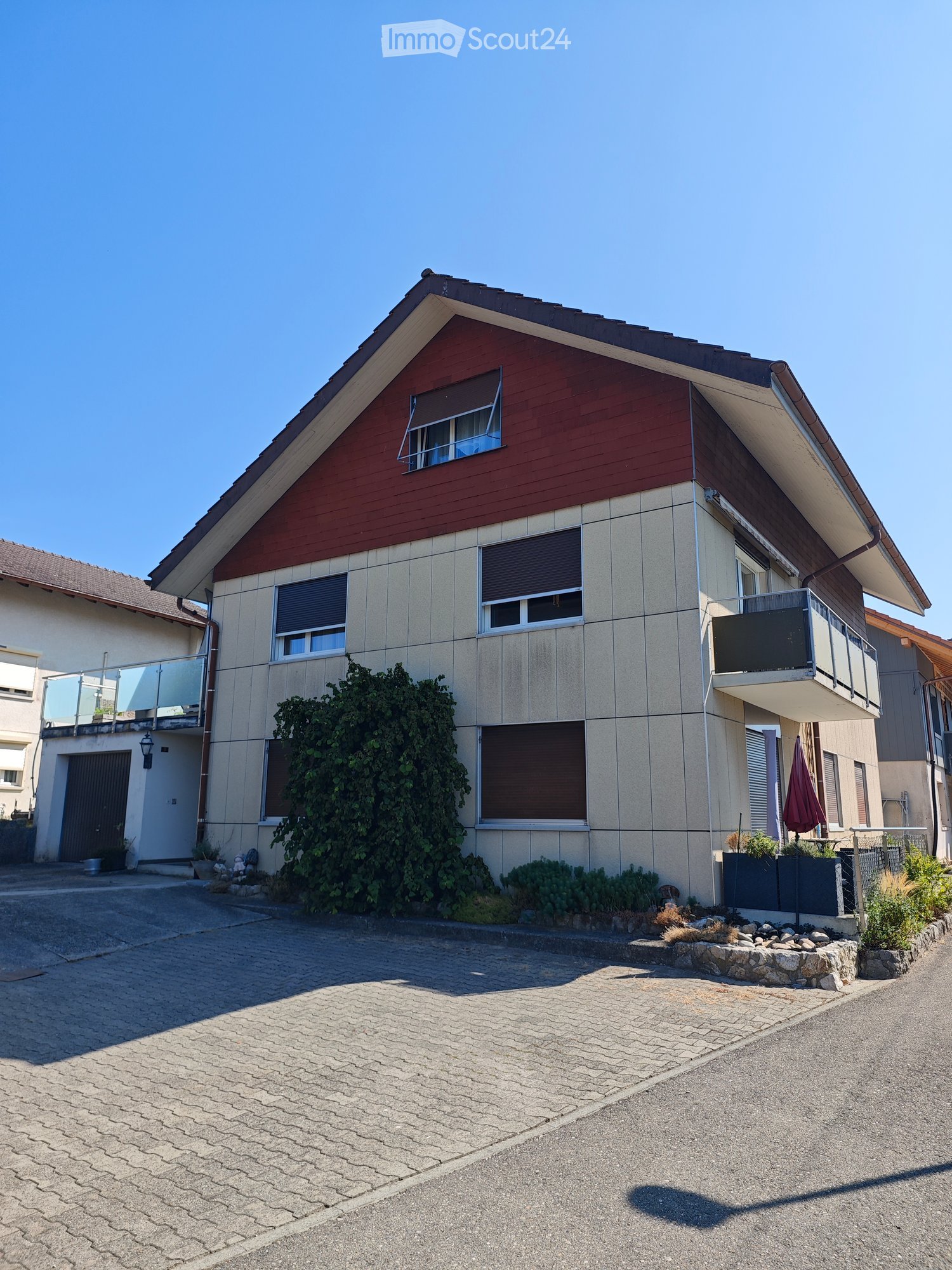 Two-story house with beige and red exterior, multiple windows with blinds, balconies, and a driveway.