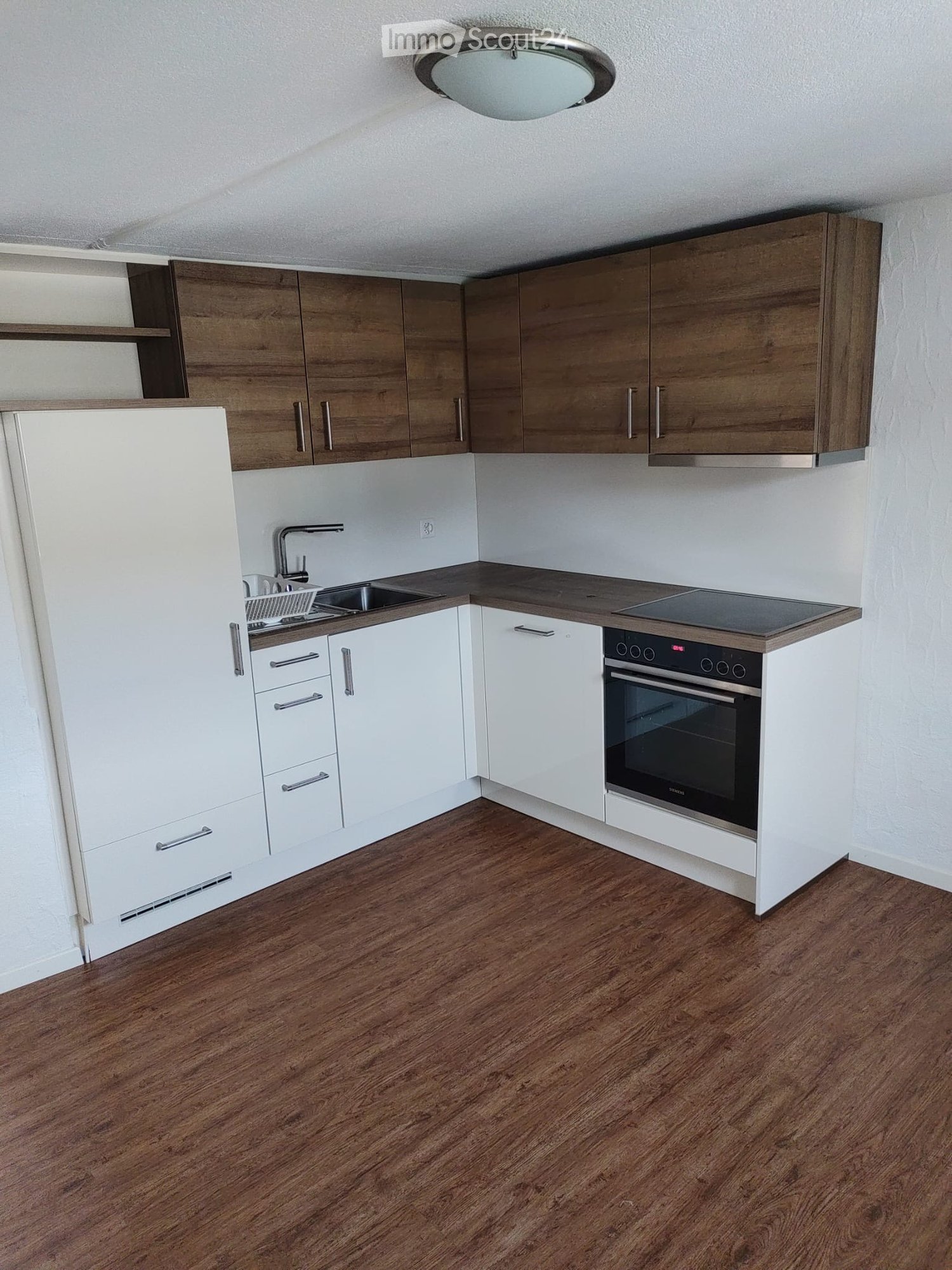 Modern kitchen with wooden and white cabinets, stainless steel sink, oven, and wooden flooring.