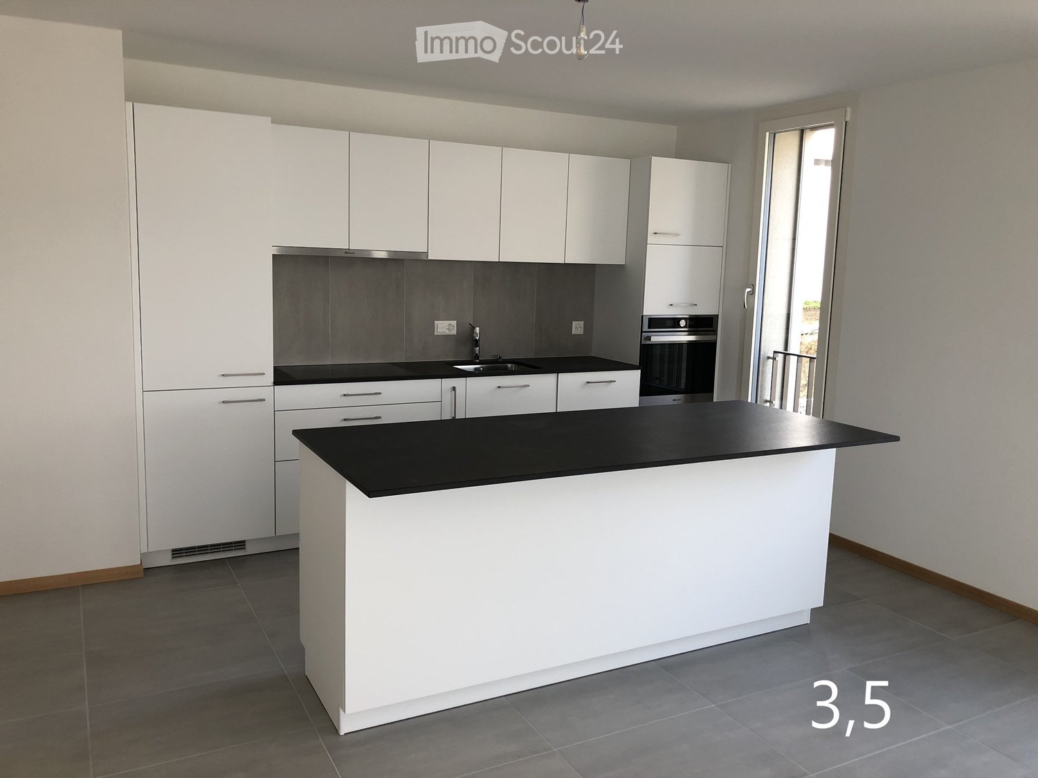 Modern kitchen with white cabinets, black countertops, and a central island. Features a sink, oven, and ample storage space.