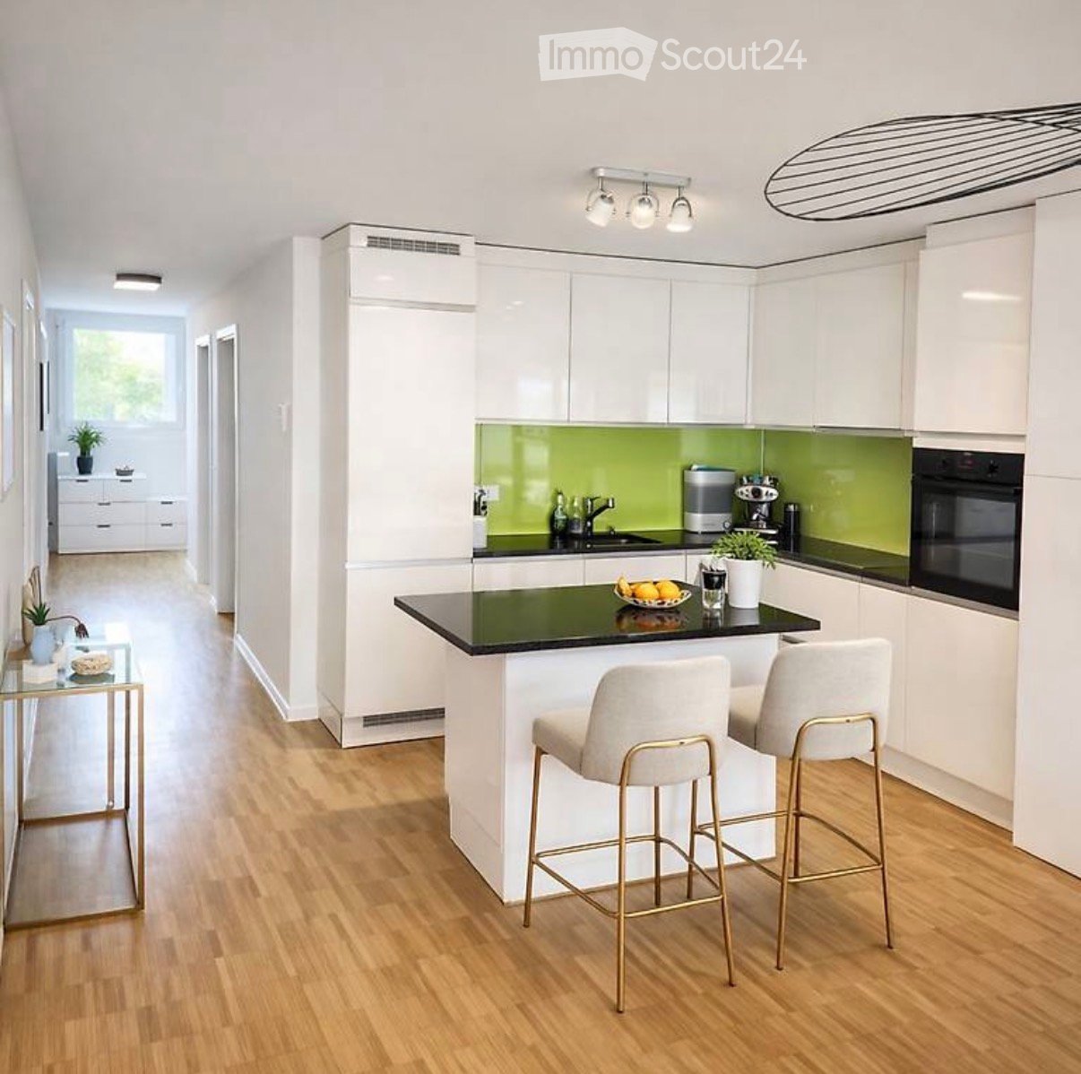 Modern kitchen with white cabinets, green backsplash, island with bar stools, and various appliances including an oven and coffee maker.