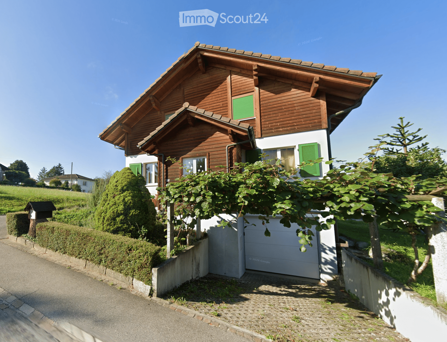 Two-story wooden house with green shutters, white garage, and well-maintained garden.