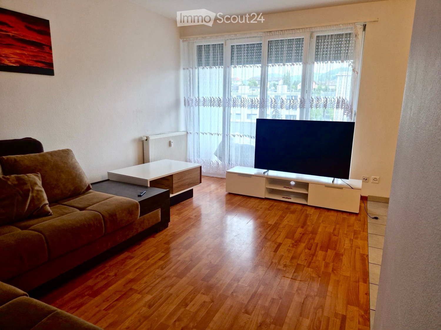 Spacious living room with hardwood floors, large windows, a sofa, a coffee table, and a TV stand with a flat-screen TV.