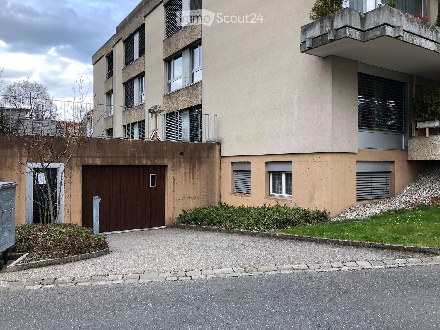 Modern multi-story residential building with a garage entrance, balconies, and large windows.
