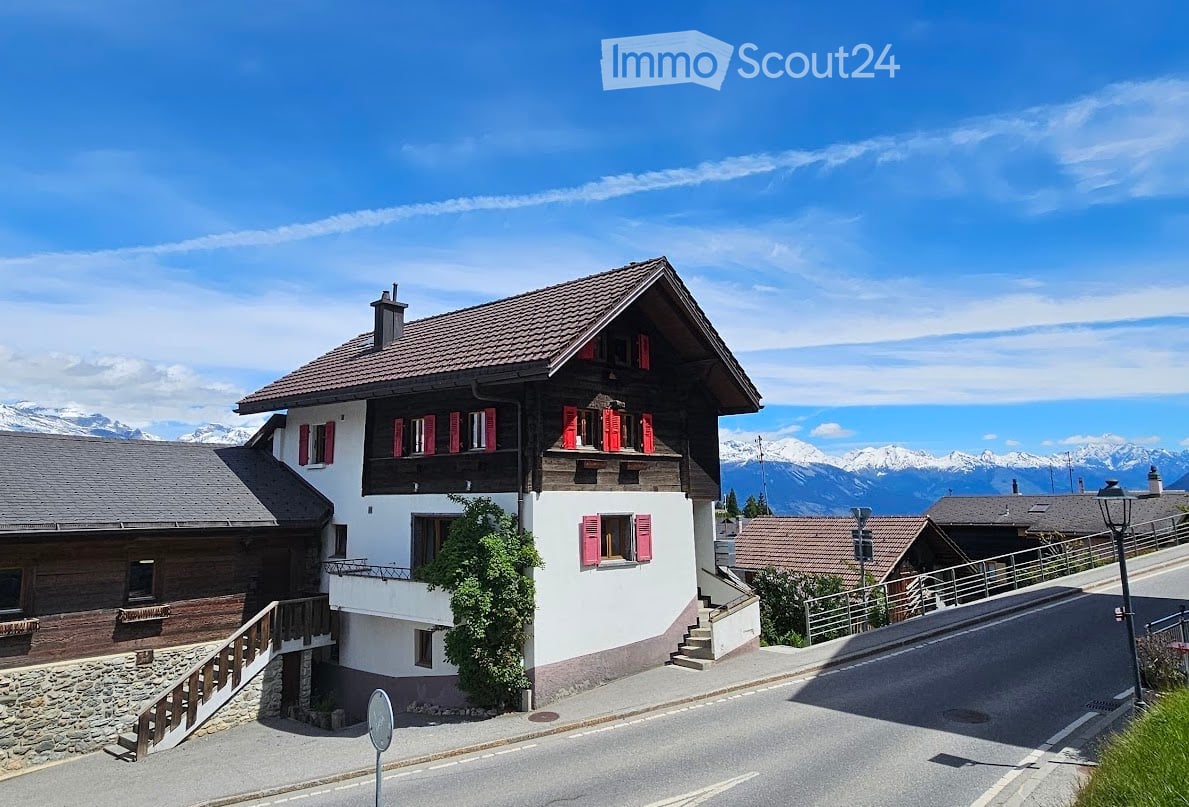 House. Traditional Swiss house with red shutters, white walls, and a tiled roof, situated in a scenic mountain landscape.