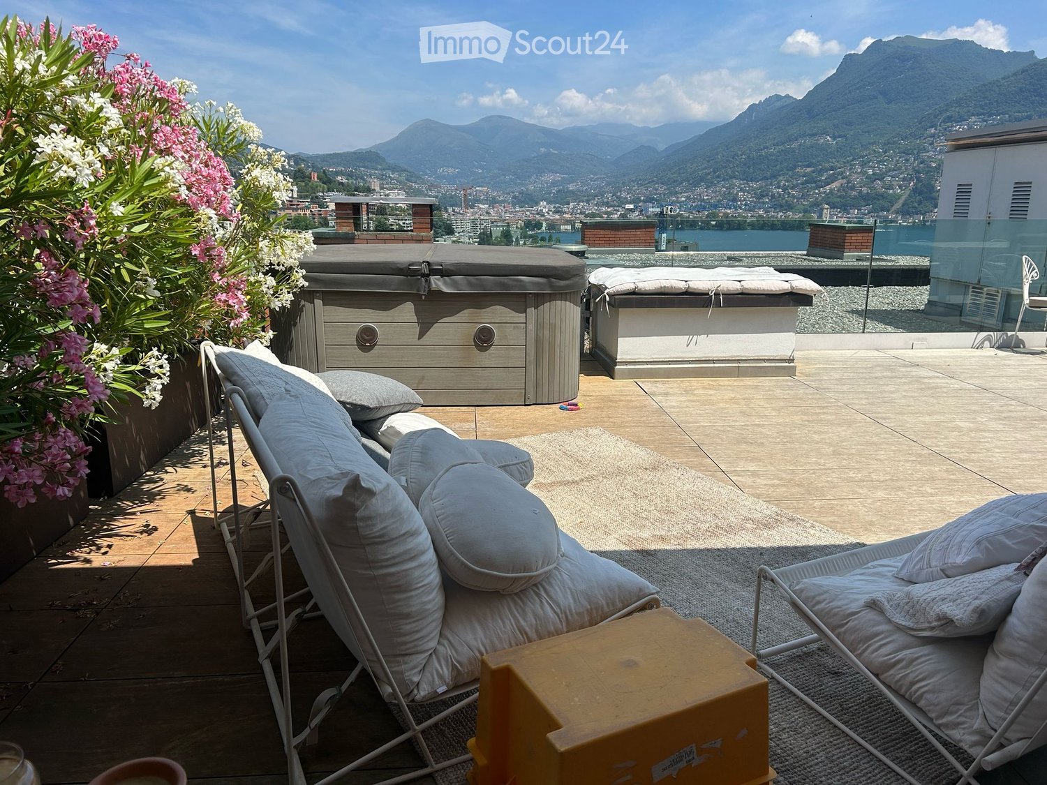 A rooftop terrace with lounge chairs, a small table, a hot tub, and a scenic mountain view.