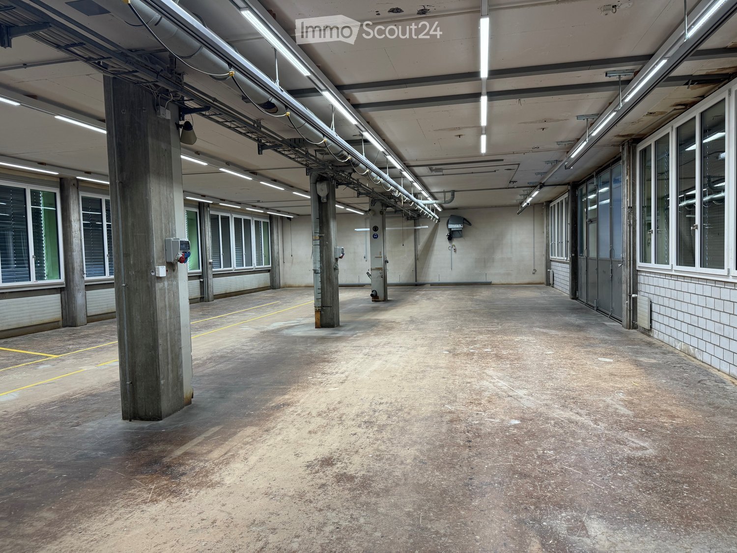 Empty industrial-style garage with concrete floors, large windows, and exposed structural beams. No furniture or equipment present.