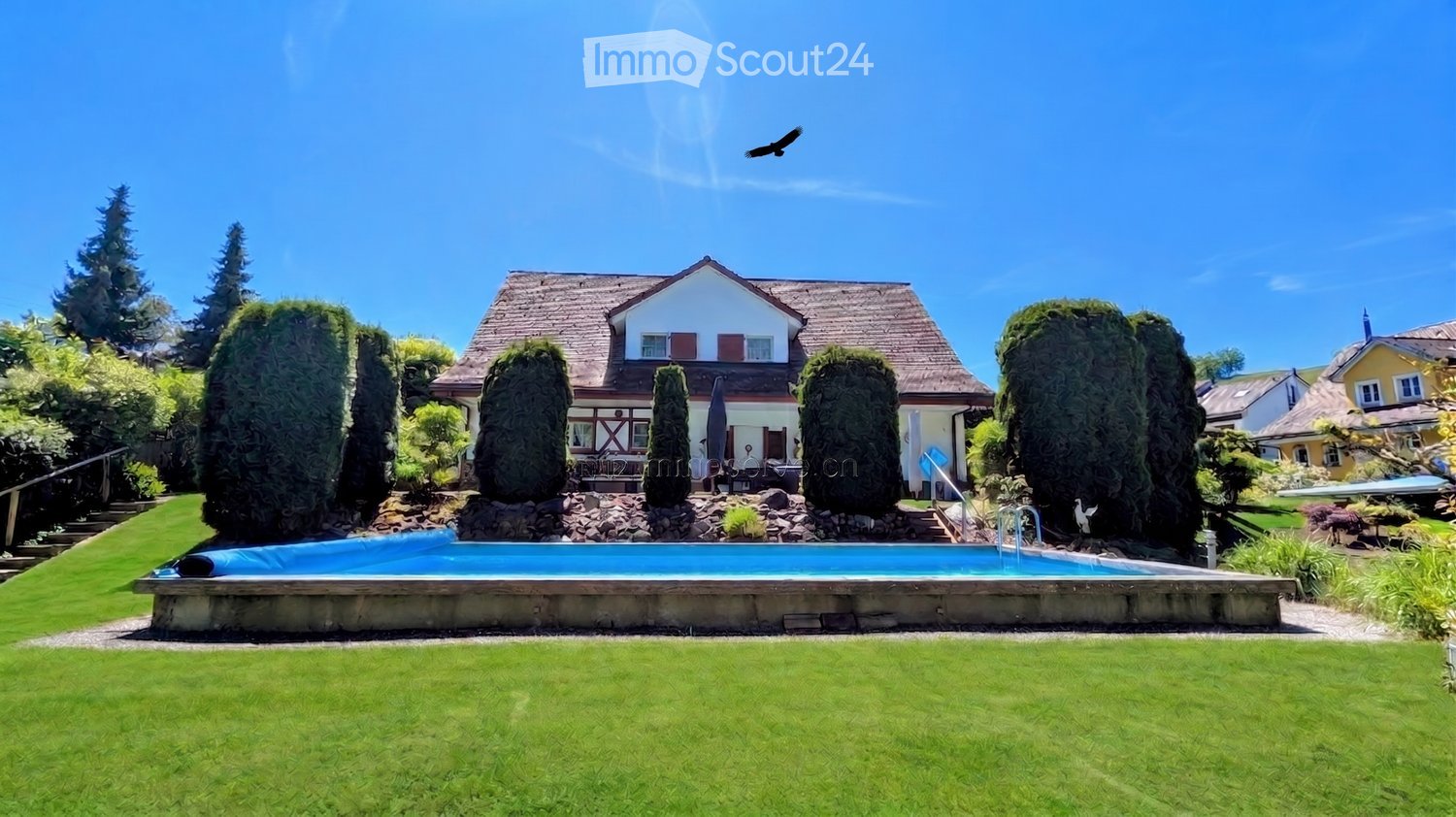 A well-maintained garden with a swimming pool, surrounded by neatly trimmed trees and a two-story house in the background.