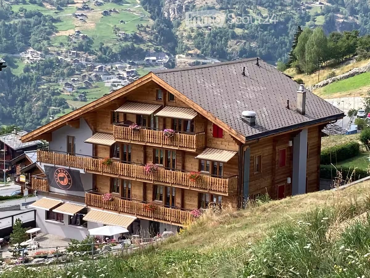 A large wooden chalet with multiple balconies and a panoramic mountain view.