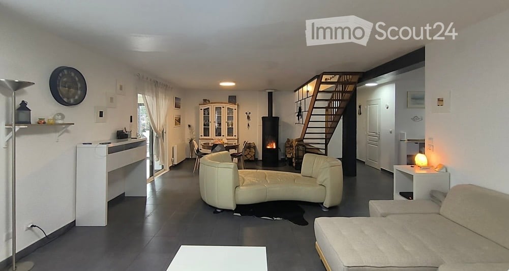 Bright living room with a fireplace, cream-colored sectional sofa, dining area with chairs and table, white cabinet, and a staircase leading to the upper level.