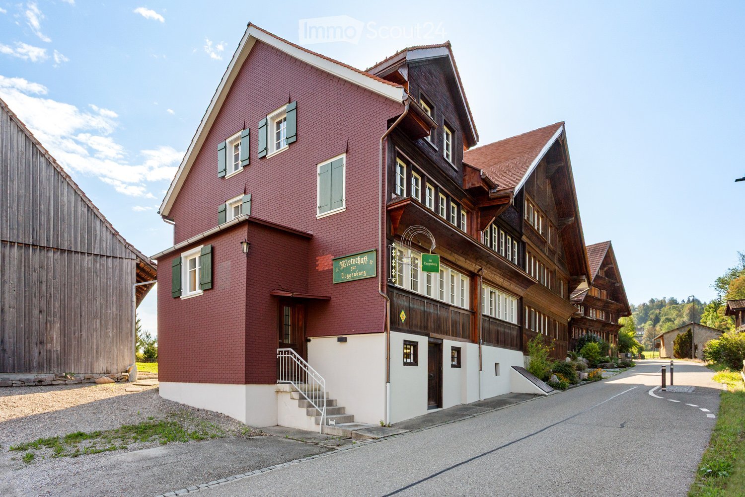A two-story building with red brick walls and green shutters, featuring a wooden balcony and a sign reading "Mietshaus zur Gögenburg".