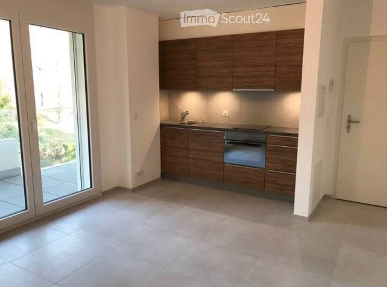 Modern kitchen with dark wooden cabinets, a sink, and an oven. The space is open and bright, with large windows and a tiled floor.