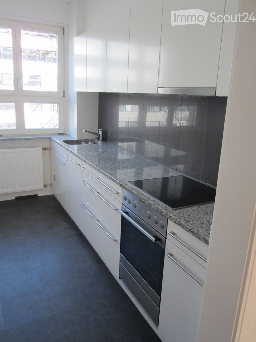 Modern kitchen with white cabinets, granite countertop, built-in oven, sink, and faucet. Large windows provide natural light.