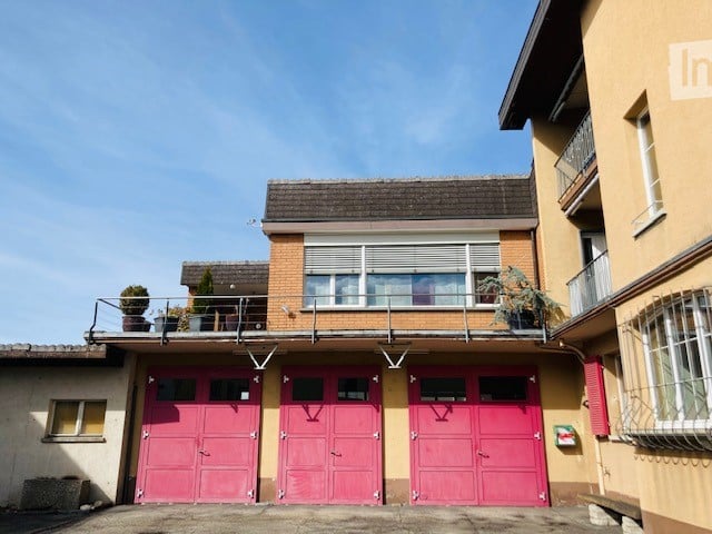Two-story building with three large pink garage doors, a balcony on the upper floor, and potted plants on the balcony railing.