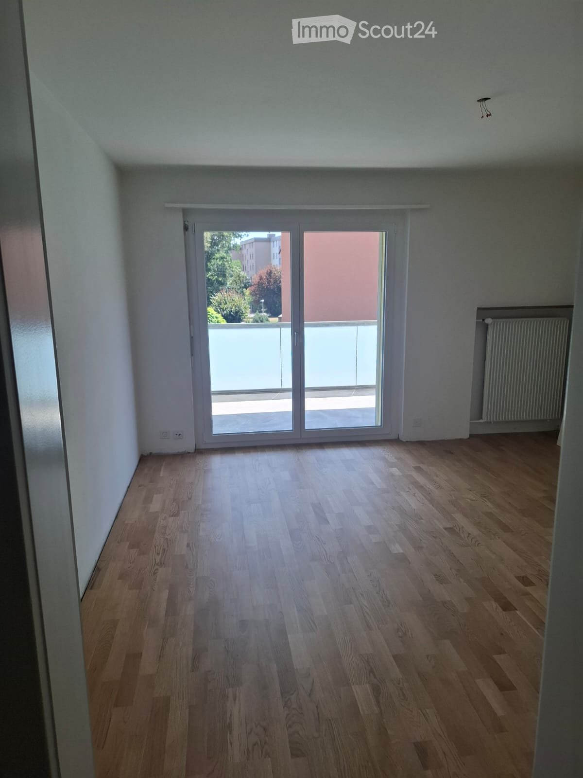 Empty room with wooden flooring, white walls, and a large sliding glass door leading to a balcony.