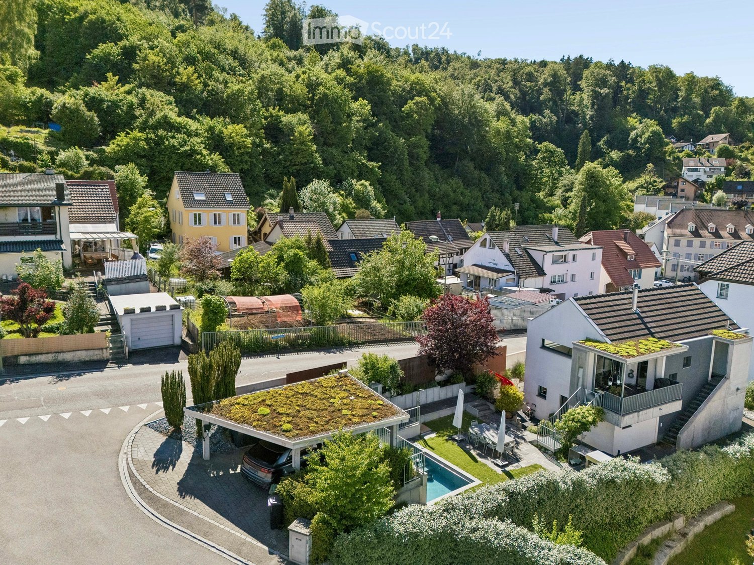 Aerial view of a residential neighborhood with multiple houses, gardens, and a swimming pool in the foreground.