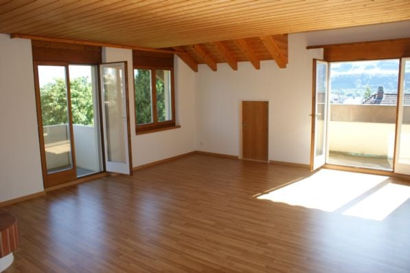 Empty room with wooden flooring, white walls, large windows, and sliding glass doors leading to a balcony.