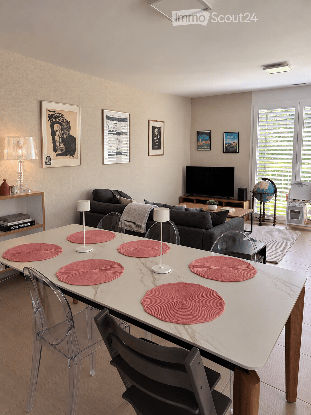 Modern living room with a white marble dining table, six chairs, a grey sofa, a television, a globe, and decorative lamps.
