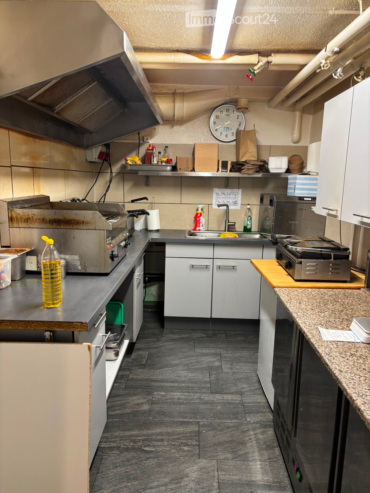 Commercial kitchen with stainless steel appliances, granite countertop, and tiled floor.