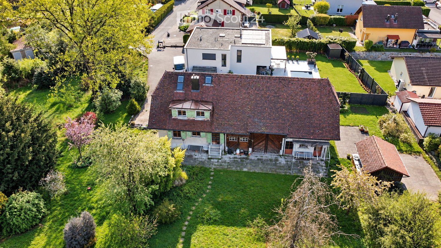Aerial view of a two-story house with a red-tiled roof, surrounded by a well-maintained garden and neighboring houses.