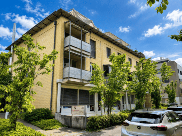 Multi-story residential building with yellow brick facade, multiple balconies, and surrounding greenery.