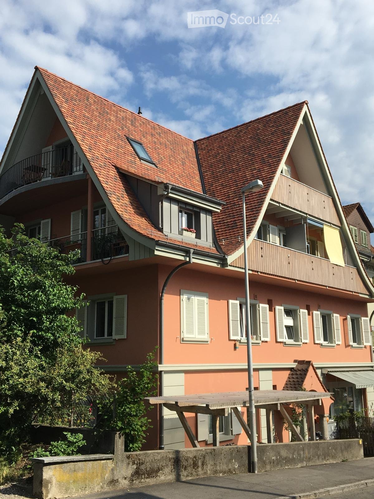 Two-story house with red-tiled roof, pink facade, white shutters, and balconies on the upper level.