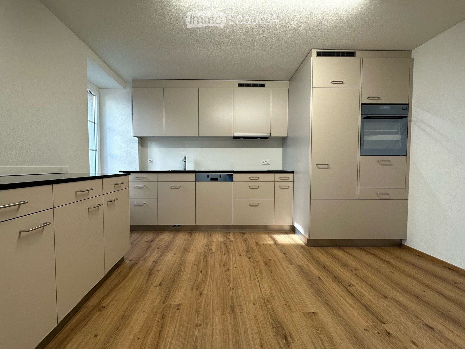 Modern kitchen with light-colored cabinets, wooden flooring, and built-in appliances including a sink and oven.