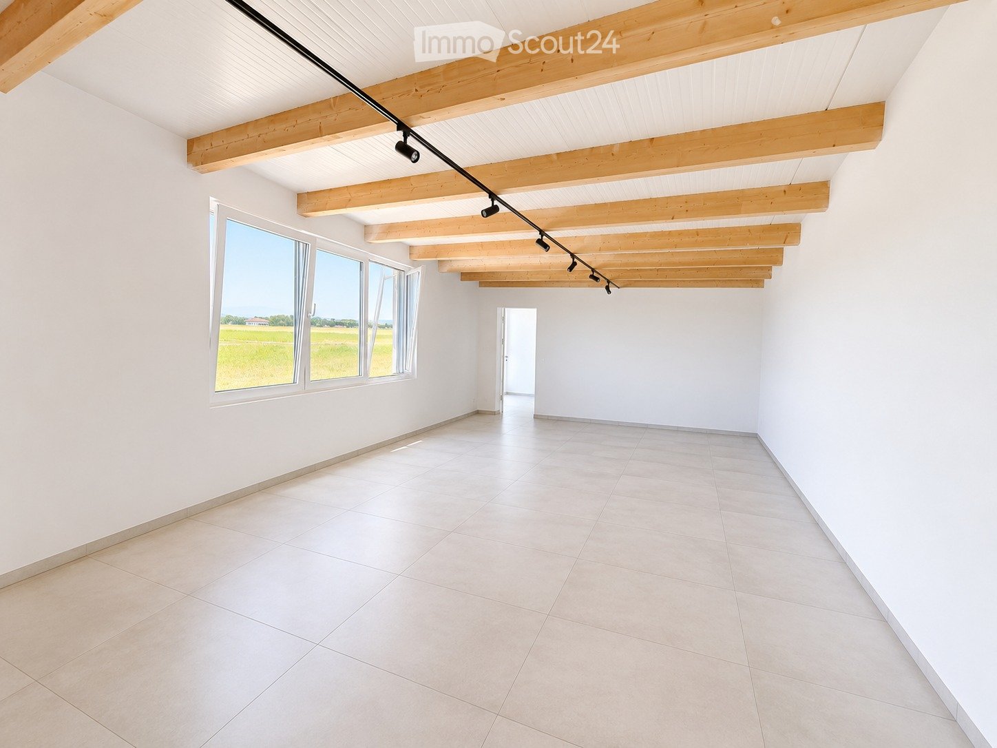 Empty room with white walls, tiled floor, large windows, and exposed wooden beams on the ceiling.