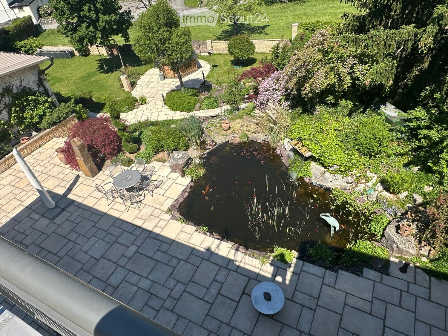 Well-maintained garden with a pond, seating area, and various plants and trees.