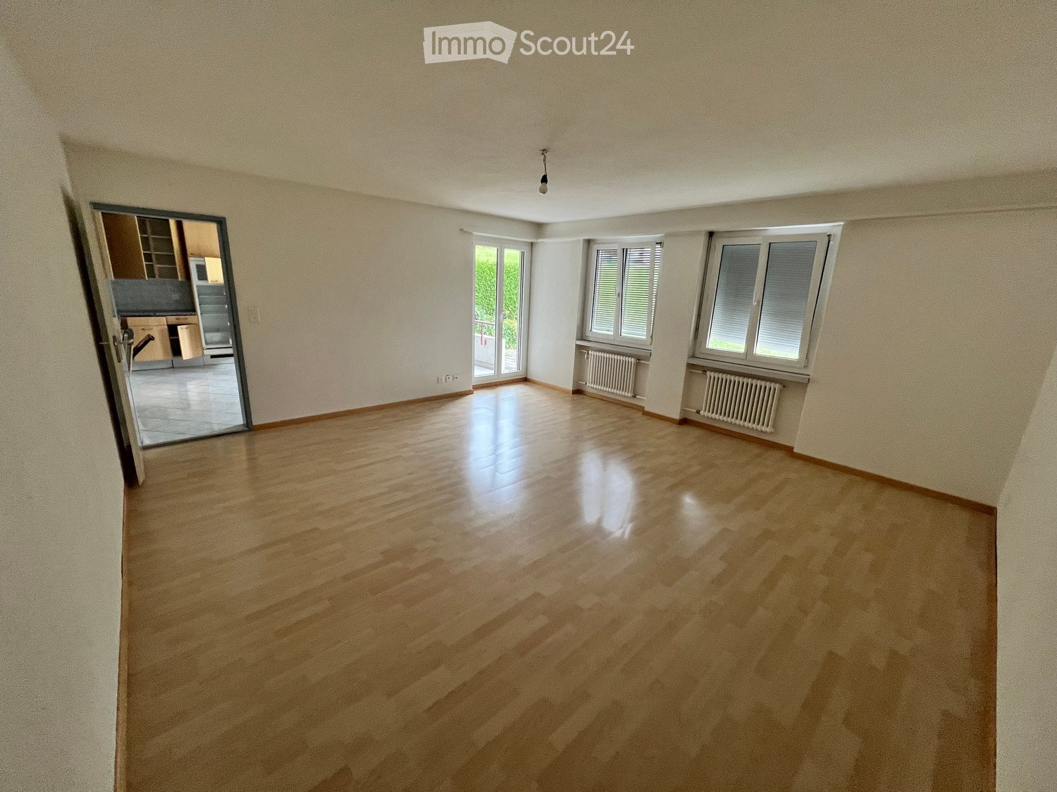 Empty room with wooden flooring, large windows, and a door leading to another room.