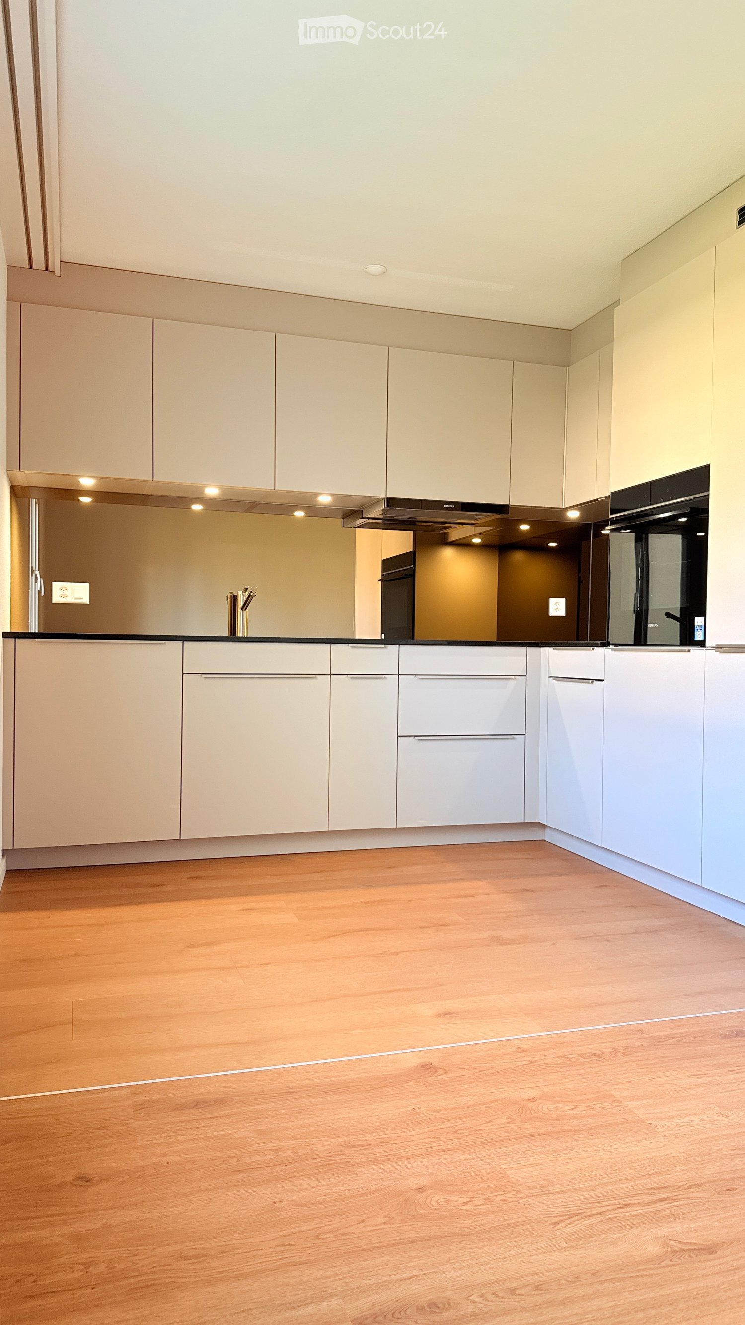 Modern kitchen with light-colored cabinets, stainless steel appliances, and a wooden floor.