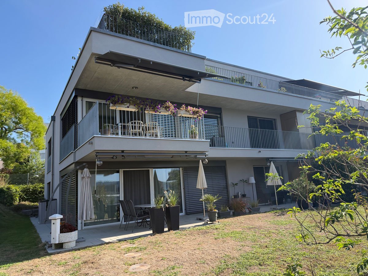 Modern two-story house with balconies, outdoor seating, and greenery.