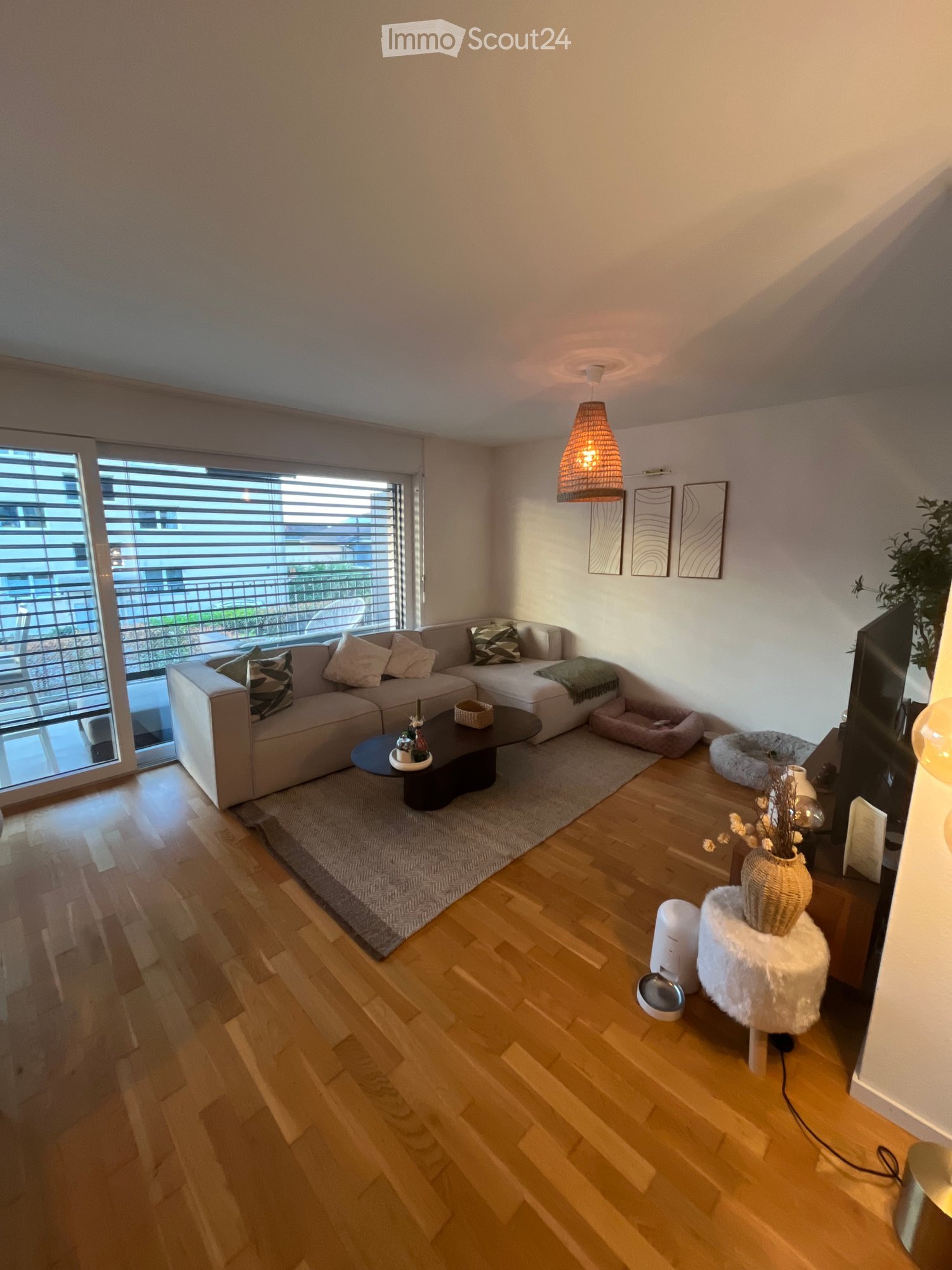 Modern living room with a sectional sofa, coffee table, floor lamp, and large windows offering a view of the city.