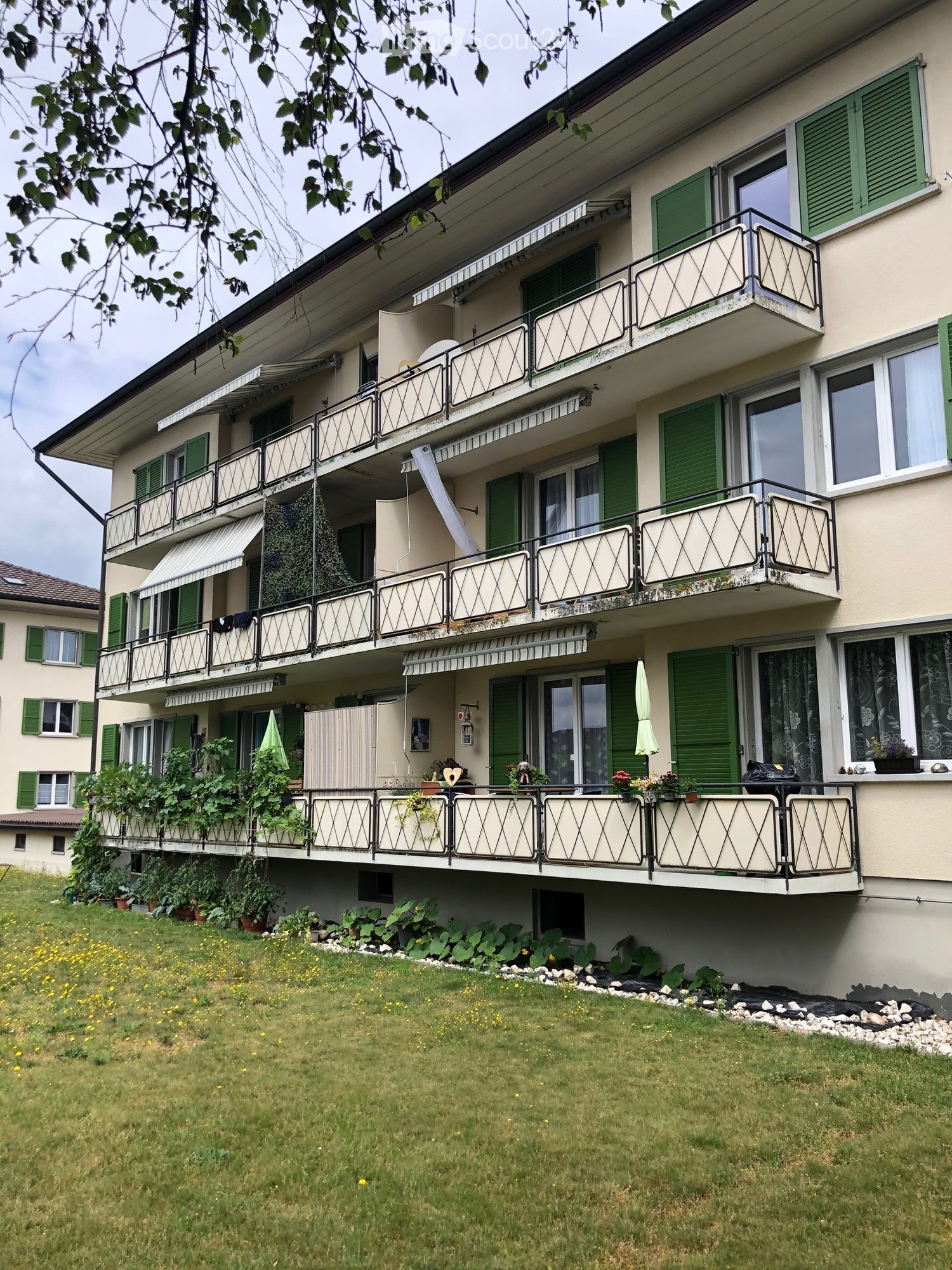 3 story building, green shutters, beige paint, multiple balconies, garden below, green grass