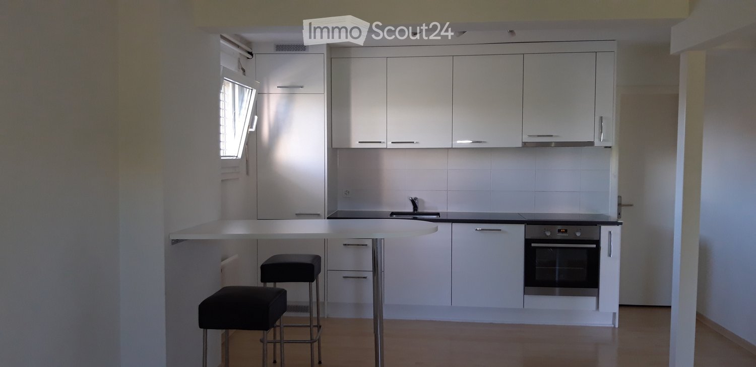 Modern kitchen with white cabinets, a central island, and two black stools. Features a sink, oven, and ample storage space.