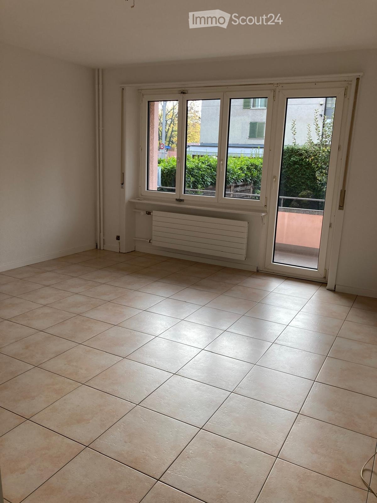 Empty room with tiled floor, large windows, radiator, and sliding glass door leading to a balcony.