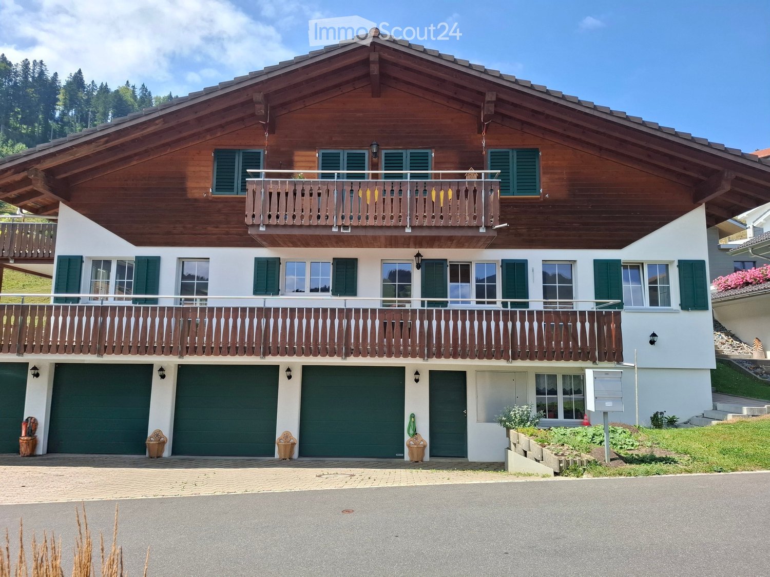 Two-story wooden house with green shutters, balconies, and multiple garage doors.