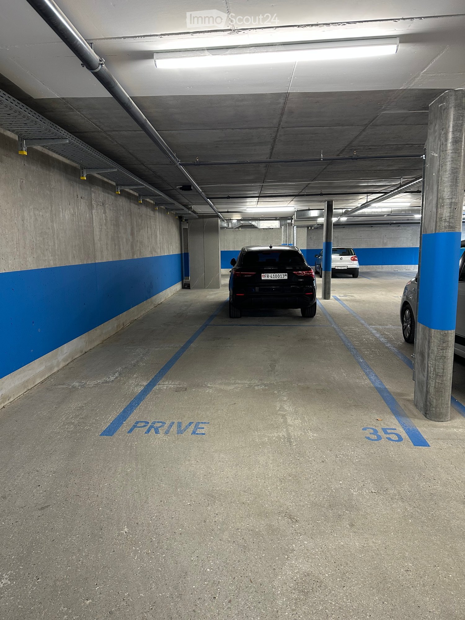 Underground parking area with marked parking spaces, concrete pillars, and a few parked cars.