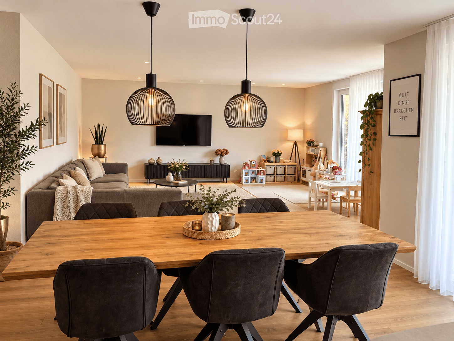 Bright, open living and dining area with wooden flooring, large windows, and modern decor. Features a grey sofa, wooden dining table with dark chairs, pendant lights, and decorative plants.