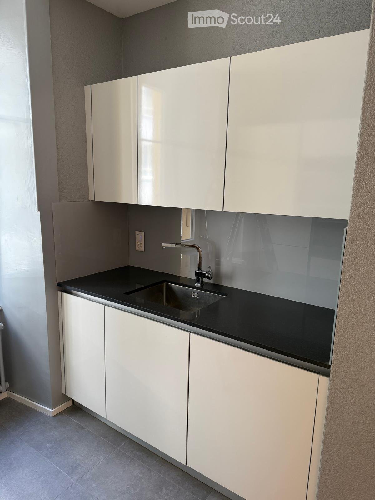 Modern kitchen with white cabinets, black countertop, and stainless steel sink.