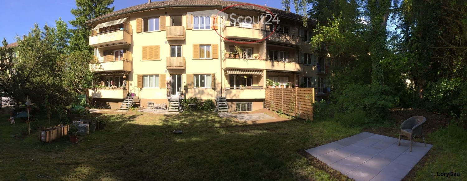 Multi-story residential building with balconies, surrounded by greenery and a well-maintained garden area.