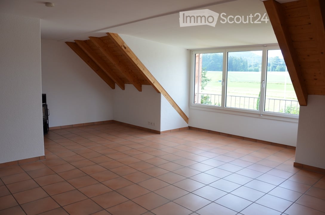 Empty room with tiled floor, white walls, large window with view, wooden beams on ceiling.