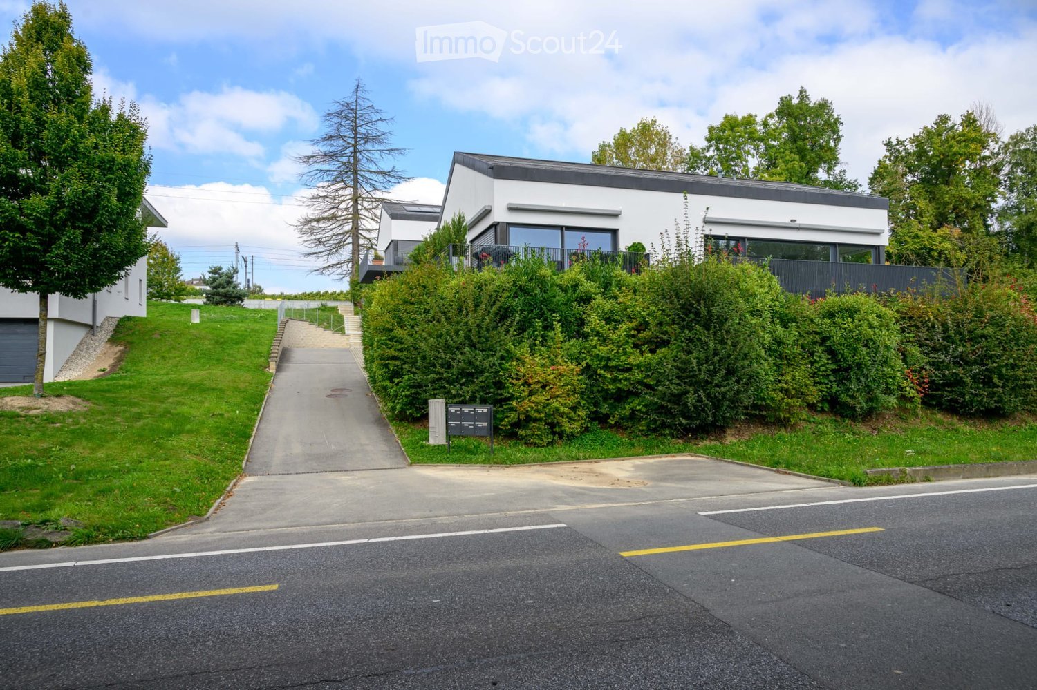House. Modern white house with a black roof, glass windows, and a driveway leading to the entrance.