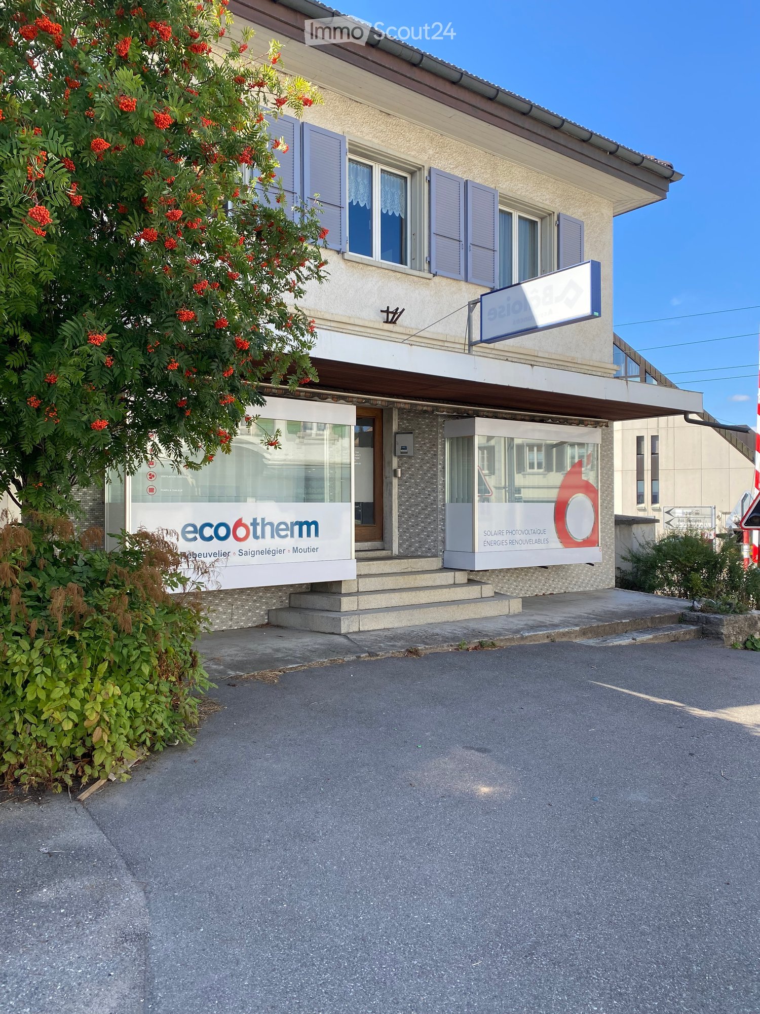 Two-story building with a storefront on the ground floor and residential apartments above. Features include a sign for "eco6therm" and a balcony with shutters.