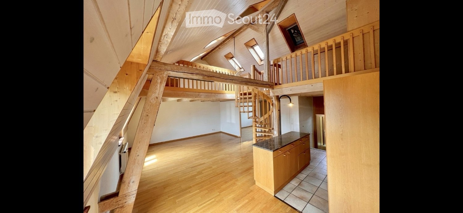 Open-plan living space with wooden floors, exposed wooden beams, a spiral staircase leading to an upper level, and a small kitchen area with a countertop and cabinets.