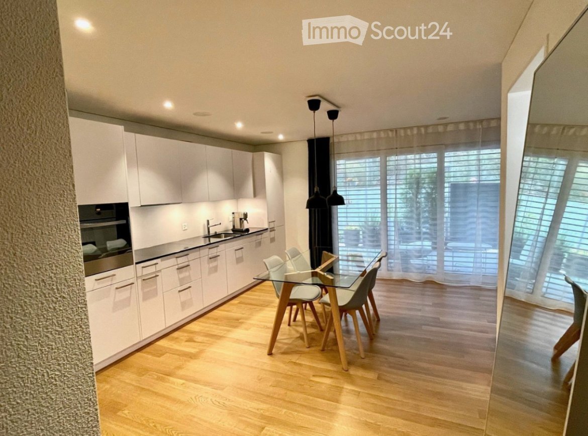 Modern kitchen with white cabinetry, stainless steel appliances, a glass dining table with wooden chairs, and large windows with blinds.