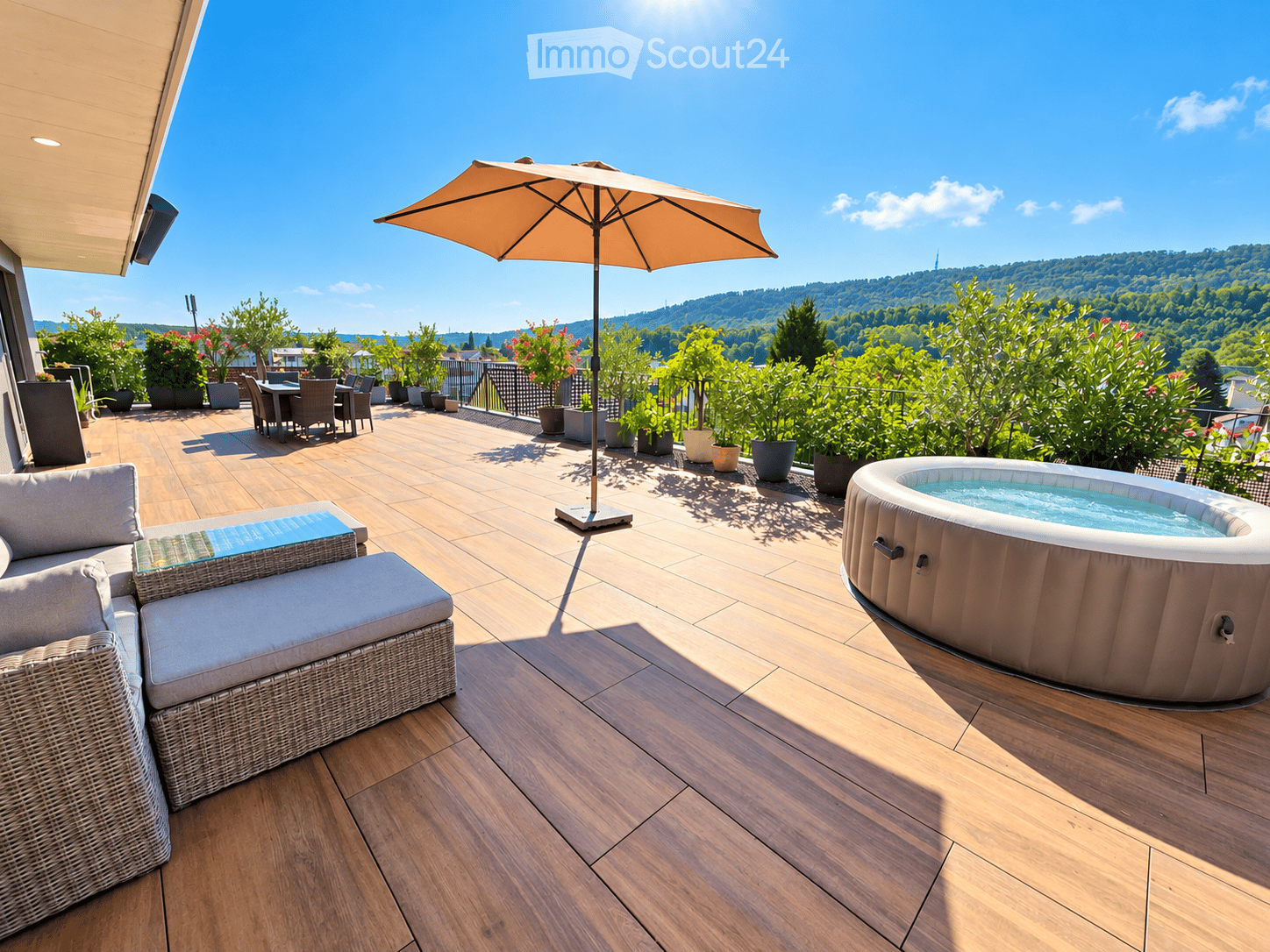 Wooden deck with a sofa, glass coffee table, dining table with chairs, umbrella, and a hot tub, surrounded by potted plants and offering a scenic view of the valley.