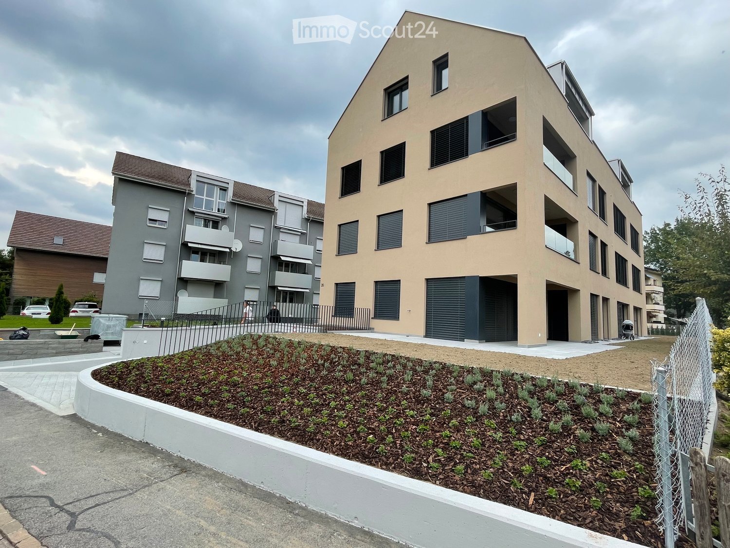Two-story residential building with modern design, multiple windows, balconies, and a landscaped garden area in front.