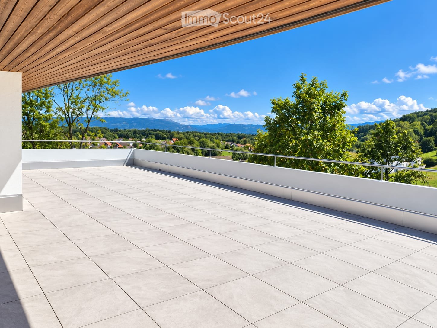 A modern balcony with a wooden roof, white tiled floor, and a metal railing, overlooking a scenic landscape with trees and distant mountains.