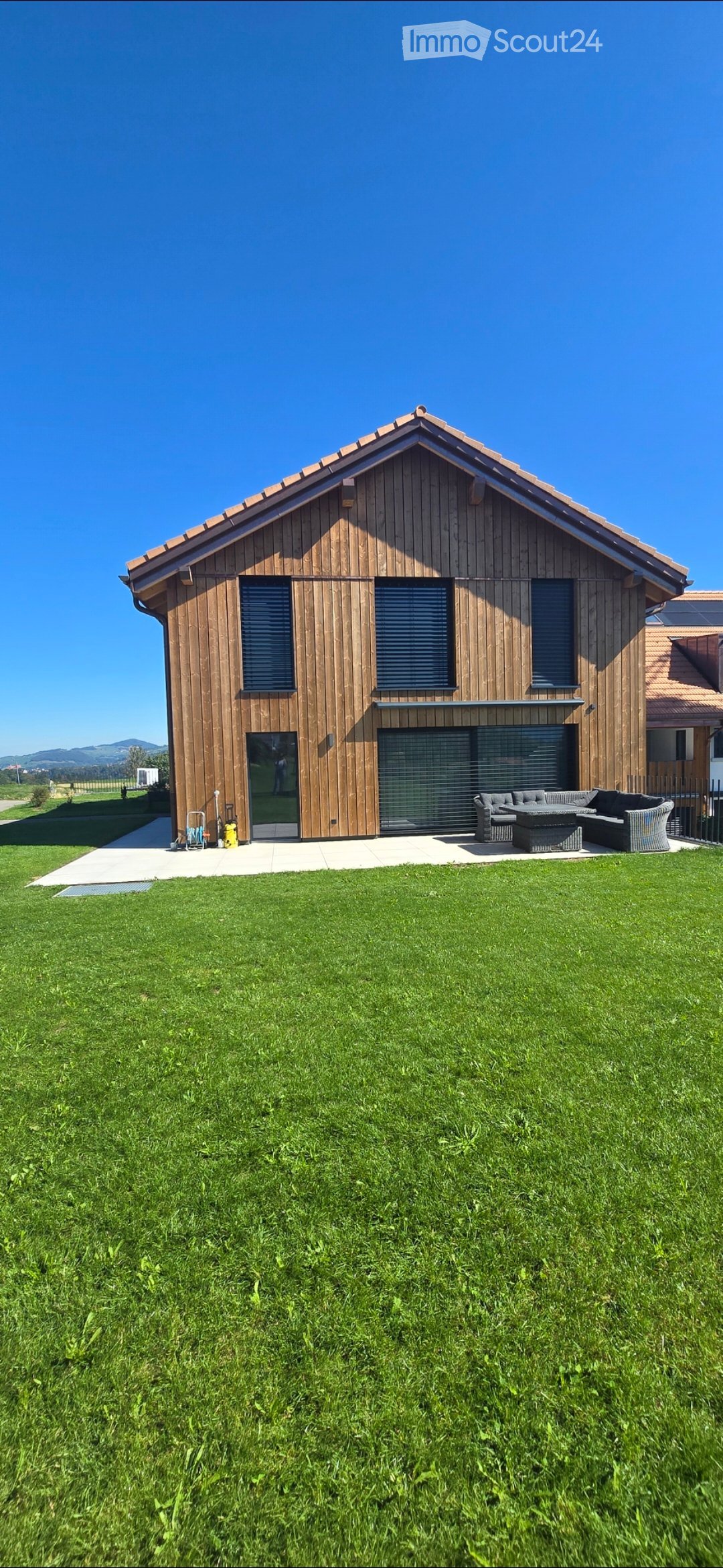 Modern two-story house with wooden exterior, large windows, garage, and outdoor seating area with sofa and table.